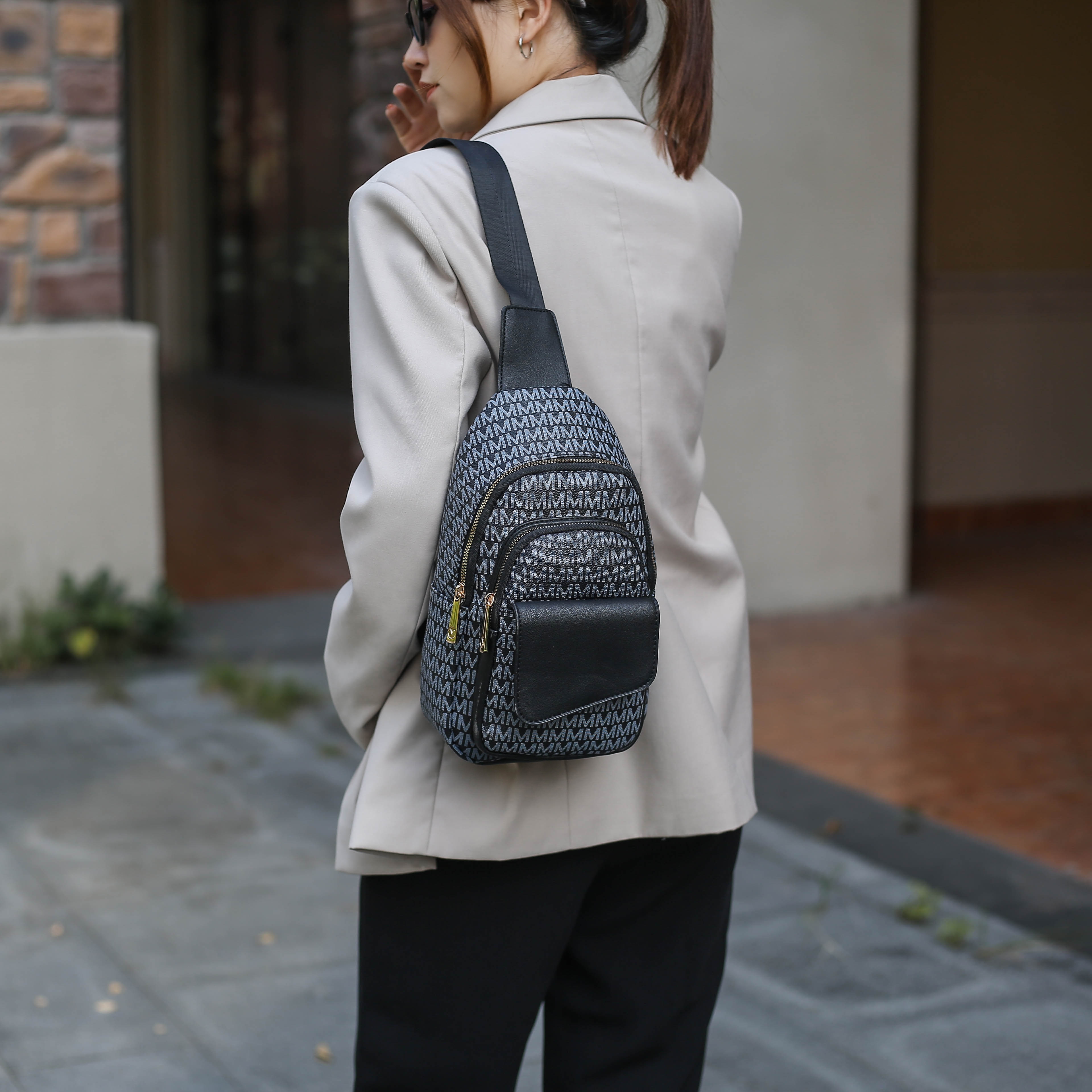 A person is wearing a light-colored blazer and black trousers, with a one-strap woven-pattern backpack.