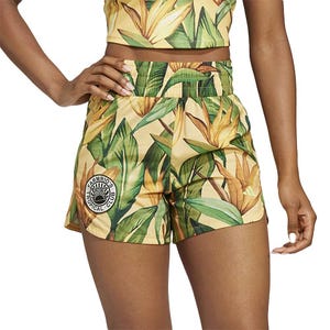 Adidas x Farm Rio Training Shorts feature a vibrant tropical leaf and flower print with a small circular logo on the left side. They have an elastic waistband and are designed for comfort and style.
