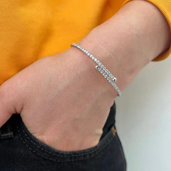 A person wearing a silver bracelet adorned with small square-cut gemstones, set against a vibrant yellow fabric and dark denim.