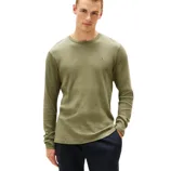 A person is wearing a ribbed, olive-green long-sleeve shirt featuring a small logo on the chest, paired with dark pants.