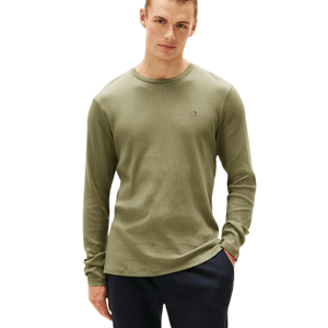 A person is wearing a ribbed, olive-green long-sleeve shirt featuring a small logo on the chest, paired with dark pants.