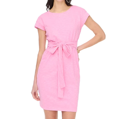 A woman is wearing a short-sleeved, knee-length pink dress with a round neckline and a matching fabric belt tied at the waist.