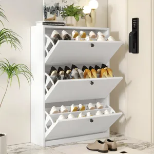 A white, multi-tiered shoe cabinet with drop-down compartments holds various shoes. It is placed next to a keypad door lock and is styled with a lamp, plant, and decorative items on top.