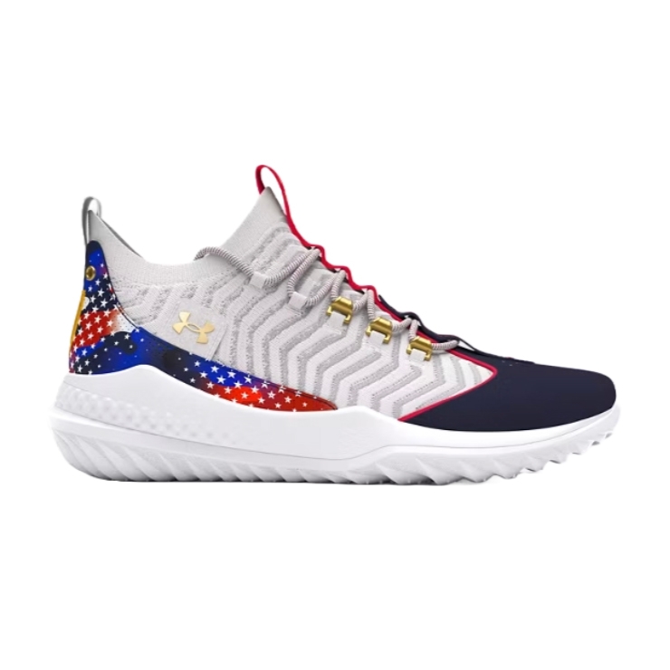 The UA Harper 9 Turf Shoes feature a light gray knit upper with chevron patterns, accented by a multicolor star-spangled design on the heel. The shoes have a white sole with a rugged texture and gold eyelets for laces.