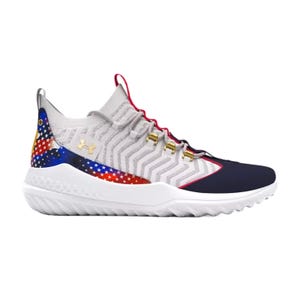 The UA Harper 9 Turf Shoes feature a light gray knit upper with chevron patterns, accented by a multicolor star-spangled design on the heel. The shoes have a white sole with a rugged texture and gold eyelets for laces.