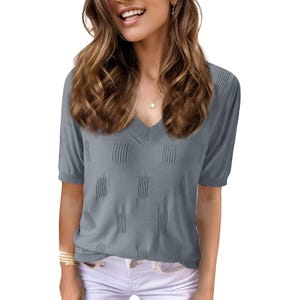 Woman wearing a gray V-neck short-sleeve top with textured patterns, paired with white pants and accessorized with a necklace and bracelets.