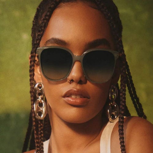A person wearing large sunglasses and silver statement earrings with braided hair.