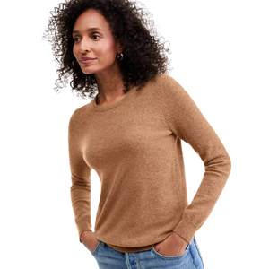 A woman wearing a brown cashmere crewneck sweater with long sleeves paired with blue jeans.