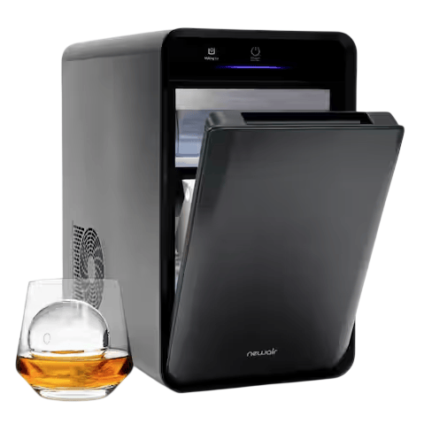 A sleek, black NewAir countertop ice maker with a top-opening lid is shown next to a glass of whiskey with a clear ice sphere.