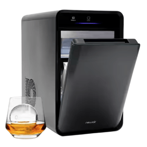 A sleek, black NewAir countertop ice maker with a top-opening lid is shown next to a glass of whiskey with a clear ice sphere.