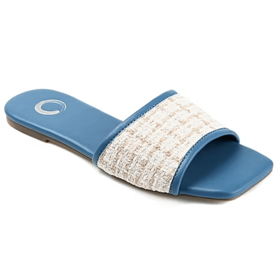 A blue slipper with a square toe and flat sole features a wide strap covered in white textured fabric, creating a stylish contrast.