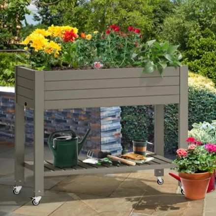 Raised garden bed on wheels with blooming flowers and gardening tools beneath, surrounded by additional potted plants on a patio.