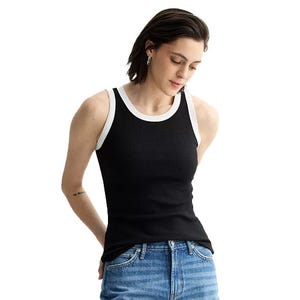 A person is wearing a black ribbed tank top with white trim paired with blue jeans.
