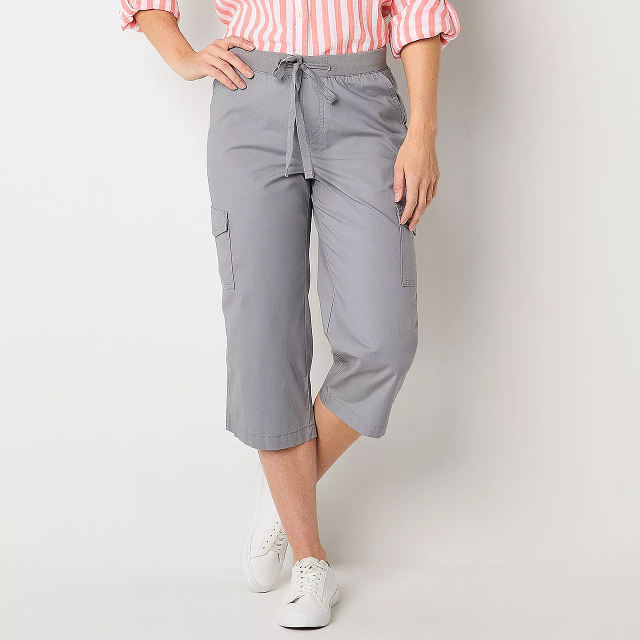 A person is wearing gray capri pants with a drawstring waist and cargo pockets, paired with white sneakers.