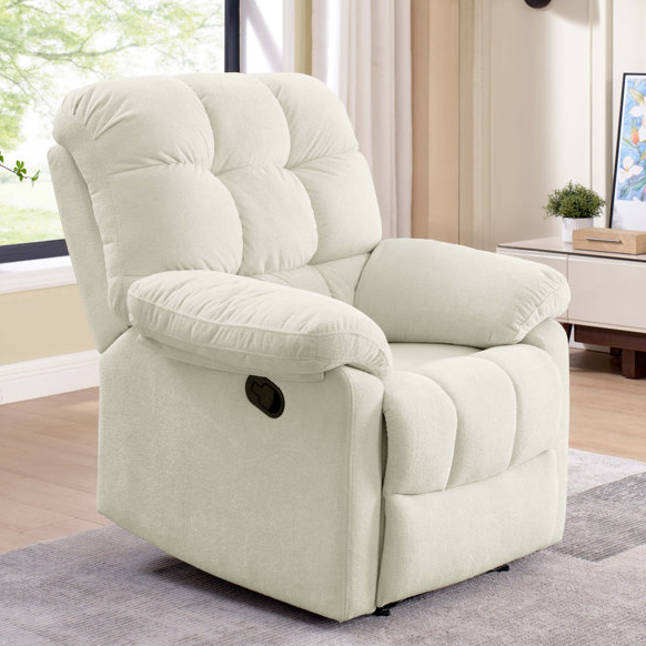 A cream-colored recliner chair with a plush, tufted design and a manual lever on the side, situated in a cozy living room setting with a window and decorative elements.
