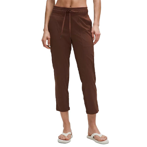 A person is modeling brown cropped pants with a drawstring waist, paired with white sandals.