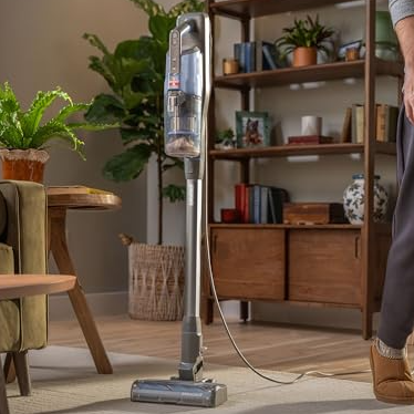 Upright vacuum cleaner with a self-standing design shown in a living room setting, emphasizing the convenience of parking and cleaning at your own pace.