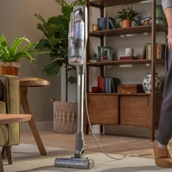 Upright vacuum cleaner with a self-standing design shown in a living room setting, emphasizing the convenience of parking and cleaning at your own pace.