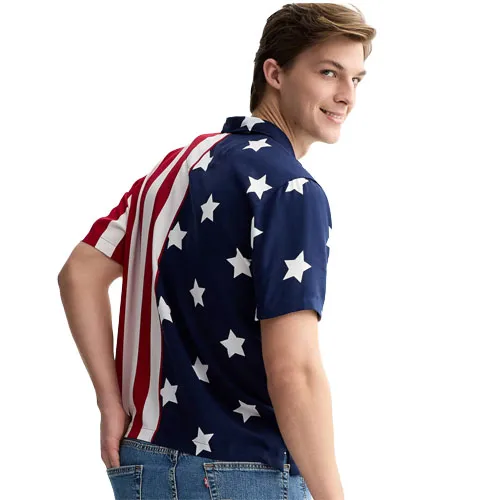 A person is wearing a short-sleeved shirt with an American flag design, featuring blue with white stars and red and white stripes, paired with blue jeans.