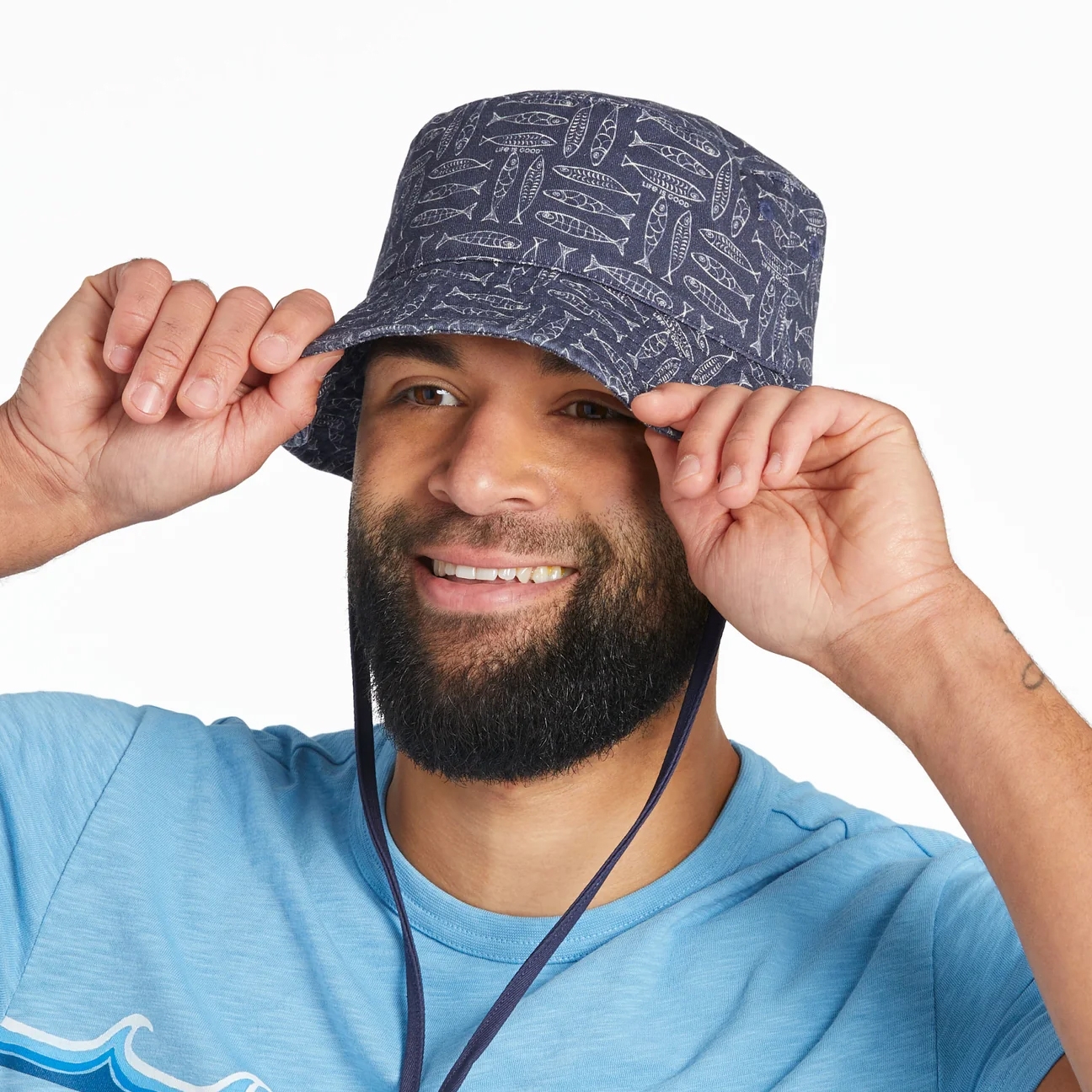 A person wears a blue bucket hat with a pattern of white fish, paired with a light blue shirt.