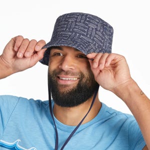 A person wears a blue bucket hat with a pattern of white fish, paired with a light blue shirt.