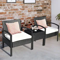 Two black rattan chairs with white cushions and red chevron-patterned pillows are connected by a small center table, set against a brick wall.