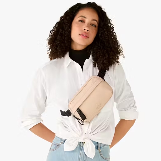 A woman wearing a white button-up shirt tied at the waist, a black turtleneck, light blue jeans, and a beige crossbody bag.