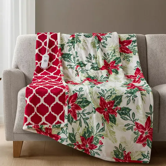 A floral-patterned, heated blanket with a red and white motif and attached control panel draped over a light gray sofa.