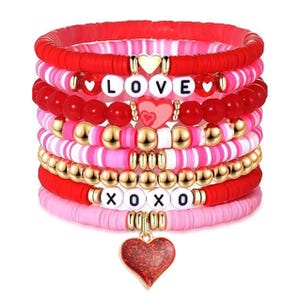Valentine's Beaded Bracelet Set features multiple red, pink, and gold bracelets with bead designs spelling \“LOVE\“ and \“XOXO,\“ including heart accents and a hanging heart charm.