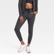 The person is wearing a black athletic jacket, a black sports bra, charcoal joggers, and white sneakers.