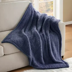A plush, dark blue sherpa throw blanket is draped over a light-colored sofa in a room with a window overlooking an outdoor scene.