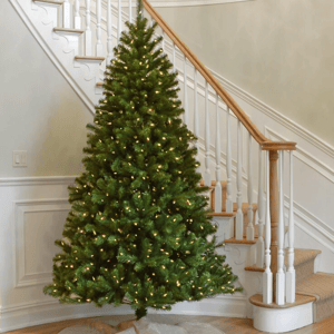 A 7.5-foot pre-lit artificial spruce tree with dense green foliage and warm white lights, set up indoors beside a staircase.