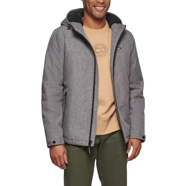 A man is wearing a gray hooded jacket over a beige sweatshirt with a logo, paired with olive green pants. The jacket has a small logo on the chest and features a zippered front and side pockets.