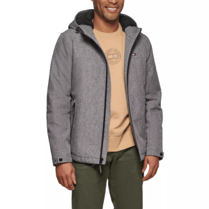 A man is wearing a gray hooded jacket over a beige sweatshirt with a logo, paired with olive green pants. The jacket has a small logo on the chest and features a zippered front and side pockets.