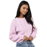 A woman wears a light pink cable-knit sweater paired with high-waisted blue jeans. She accessorizes with silver hoop earrings and rings.