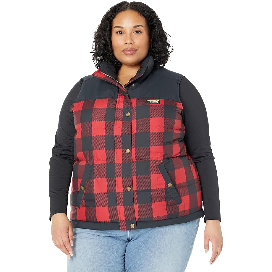 A plus-size woman is wearing a red and black buffalo plaid vest with a navy-blue stretch panel on the sides; the vest has a button-up front and two pockets.