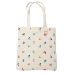 A cream-colored tote bag with a floral pattern featuring various colorful flowers. The bag includes dual handles and a small round charm attached to a ring near the top.