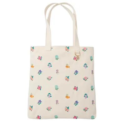 A cream-colored tote bag with a floral pattern featuring various colorful flowers. The bag includes dual handles and a small round charm attached to a ring near the top.