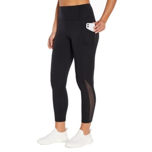 Black leggings with a high waistband, side pocket holding a phone, mesh panel details on the lower leg, paired with white athletic shoes.