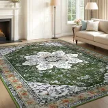 A green and white floral patterned area rug is laid on a living room floor, surrounded by a fireplace, sofa, and lamps. The rug features an intricate design with a central floral motif and decorative borders.