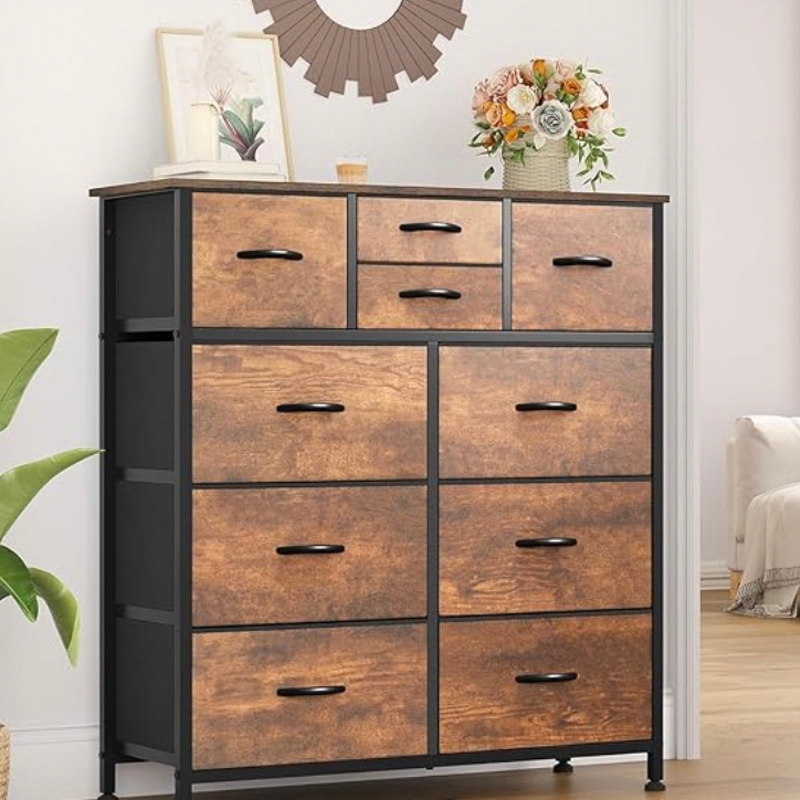 A wooden dresser with a black frame featuring multiple drawers, adorned with black handles. It is decorated with a vase of flowers and framed pictures on top.