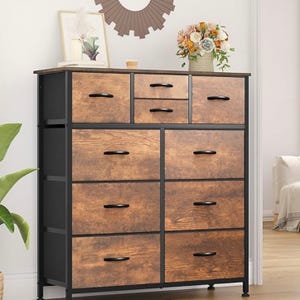 A wooden dresser with a black frame featuring multiple drawers, adorned with black handles. It is decorated with a vase of flowers and framed pictures on top.