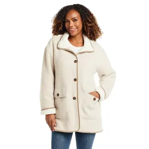 A woman is wearing a cream-colored herringbone coat with large buttons, a collar, and pockets. The coat features a cozy, sherpa-style lining and trim, and she pairs it with blue jeans.