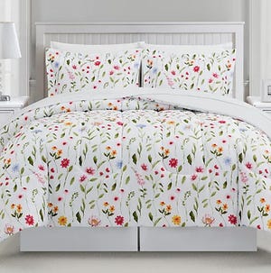 A floral-patterned comforter set featuring colorful flowers on a white background, including a comforter and two matching pillow shams, displayed on a bed.