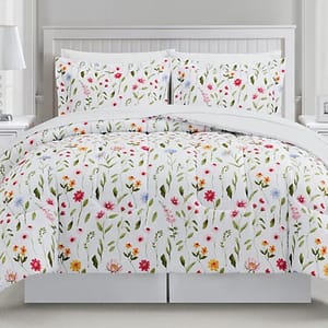 A floral-patterned comforter set featuring colorful flowers on a white background, including a comforter and two matching pillow shams, displayed on a bed.
