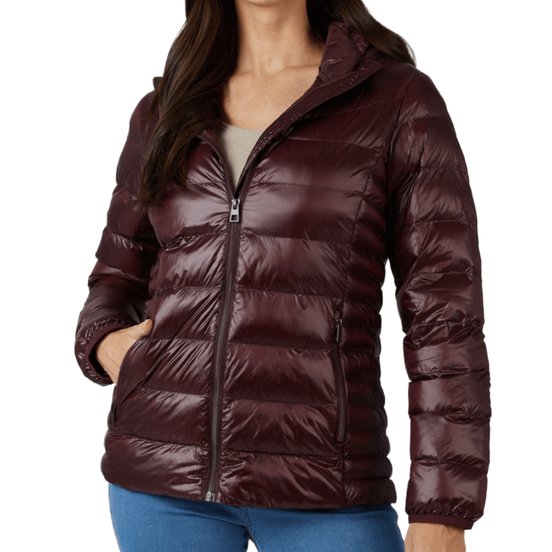 A woman is wearing a burgundy puffer jacket with horizontal quilting, a zip-up front, and side pockets, paired with blue jeans.