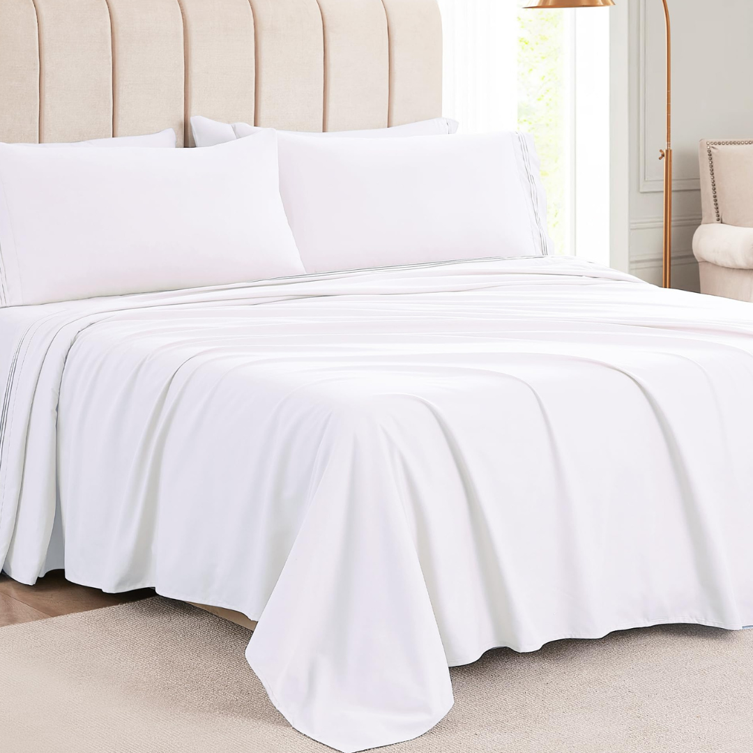 Luxurious white bed sheets and pillowcases are neatly arranged on a beige upholstered bed with a modern design, next to a gold floor lamp and cream-colored armchair.