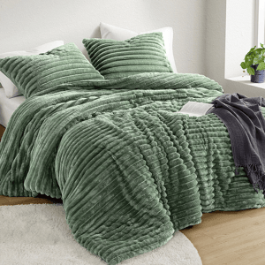 A textured green Queen Plush Comforter Set includes a ribbed comforter and matching pillow shams, creating a cozy and inviting bedroom aesthetic. A gray throw is draped over the bed, and a potted plant decorates the corner by the window.