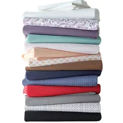 A stack of folded bed sheets in various colors and patterns, featuring shades of white, floral, purple, mint, peach, beige, brown, blue, red, gray, and black.