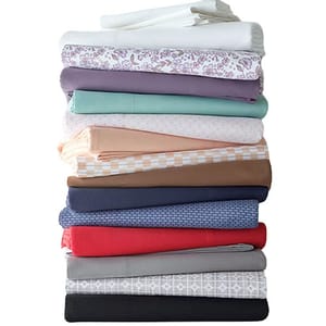 A stack of folded bed sheets in various colors and patterns, featuring shades of white, floral, purple, mint, peach, beige, brown, blue, red, gray, and black.